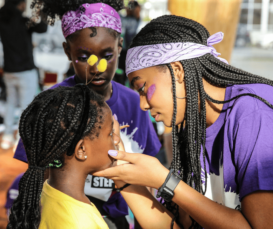 Summer Steps with Step Afrika! Purple Team member applies face paint to one of the Yellow Team members for the culminating step show.