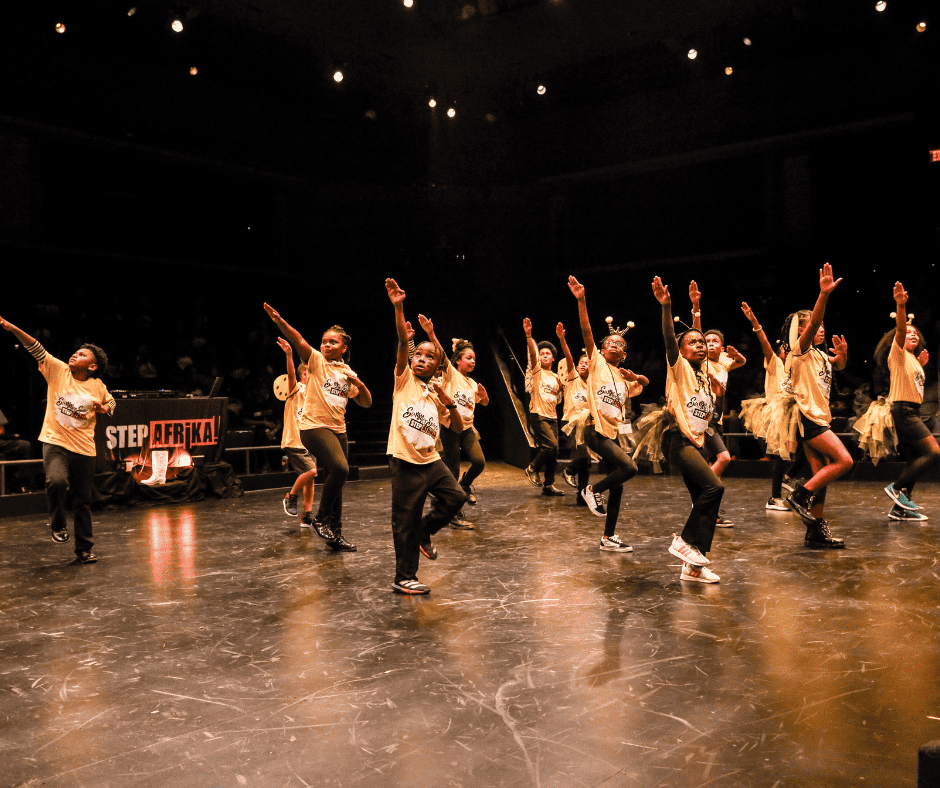 Summer Steps with Step Afrika!'s Yellow Team performing during the culminating step show. The dancers are in yellow shirts and wearing bee costumes, right arms extended into the air.